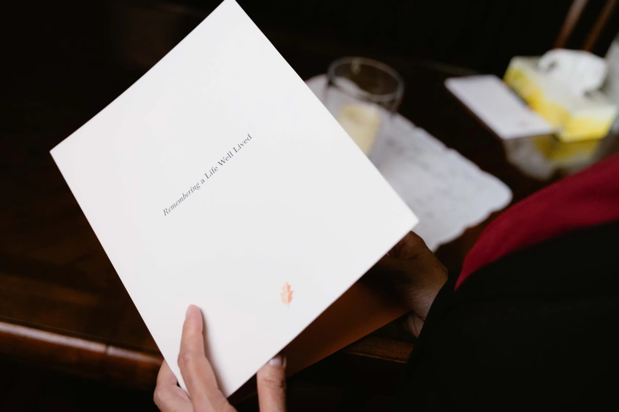 Hands holding a "Remembering a Life Well Lived" memorial folder